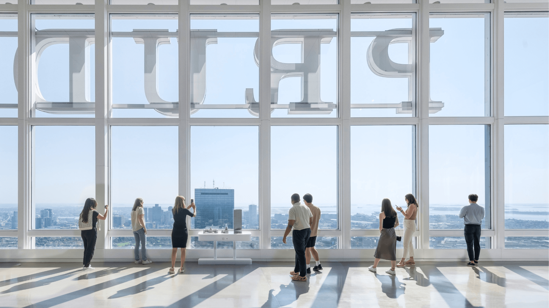 People standing at floor-to-ceiling windows viewing a cityscape from a high-rise observation deck