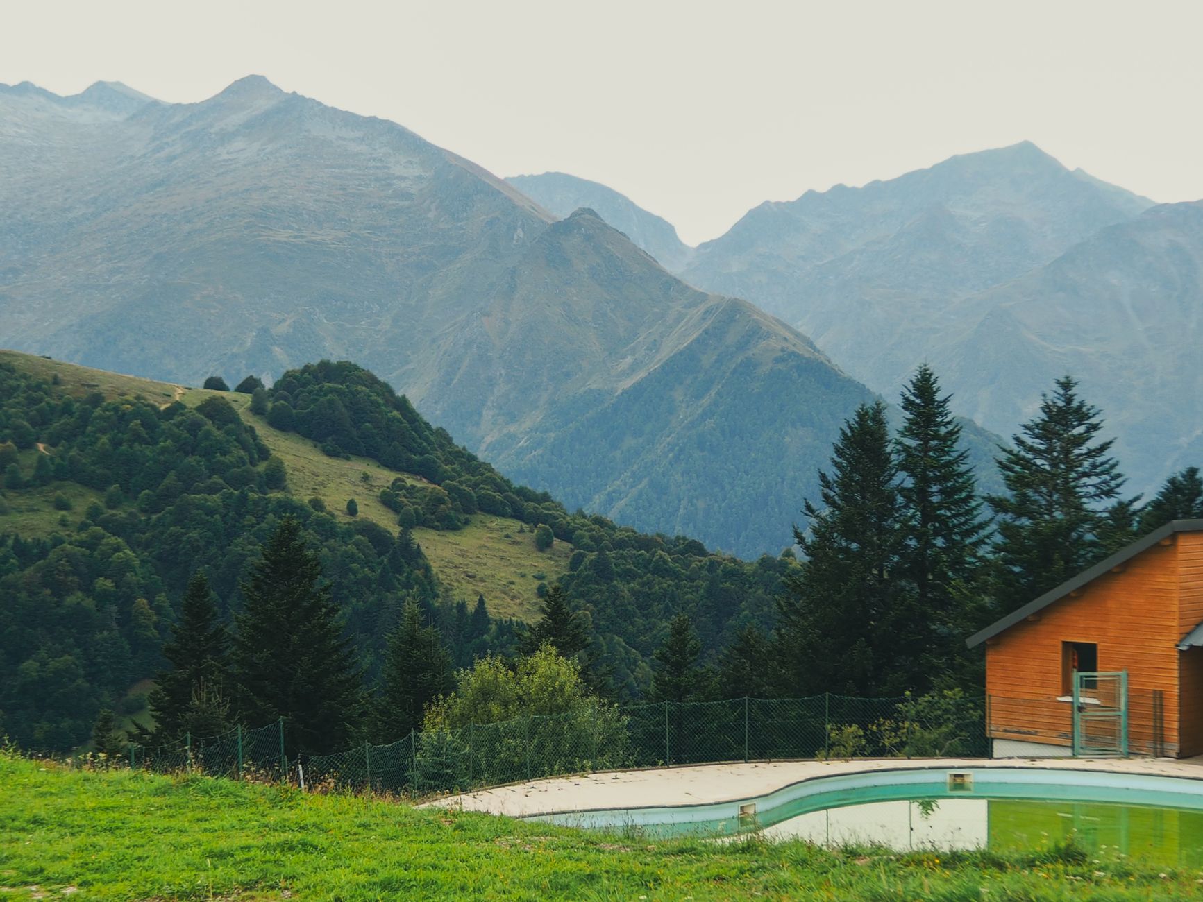 Maison orange avec piscine verte, terrasse et vue panoramique sur montagnes boisées