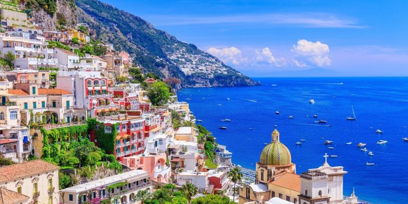 Colorful hillside village with pastel buildings and a golden dome overlooking a deep blue Mediterranean