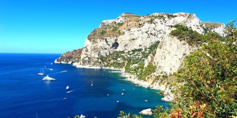 Limestone cliff face with sailboats anchored in turquoise water below