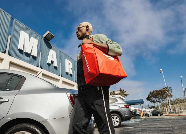 Man carrying a red insulated delivery bag outside a shopping center