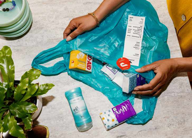 Hands holding open teal reusable shopping bag displaying groceries and household items inside